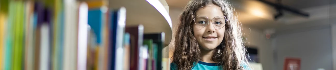 Estudante do Ensino Fundamental Anos Iniciais de Bernoulli segurando um livro, sorrindo enquanto olha para a câmera