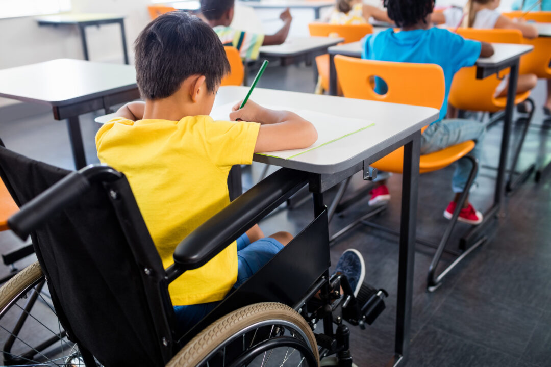 Criança em cadeira de rodas sentada à mesa da escola. 