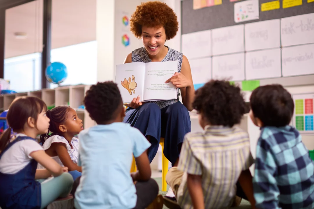 Professora negra conduz leitura para um grupo de crianças em sala de aula, promovendo a valorização da diversidade cultural e o estímulo à educação inclusiva.